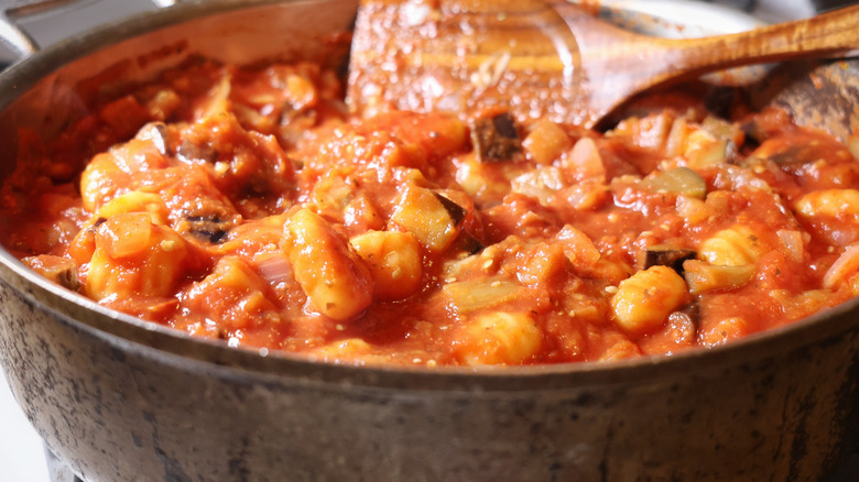 pan of gnocchi, eggplant, and onions with wooden spoon in it