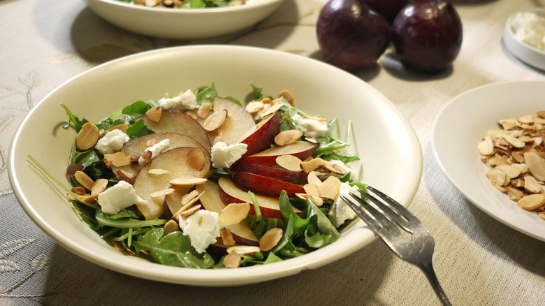 an arugula salad with chèvre, plums, and almonds on a table with plums and sliced almonds