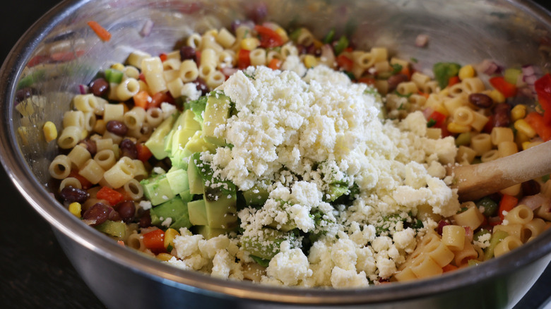 mixing bowl of pasta salad topped with avocado and cotija