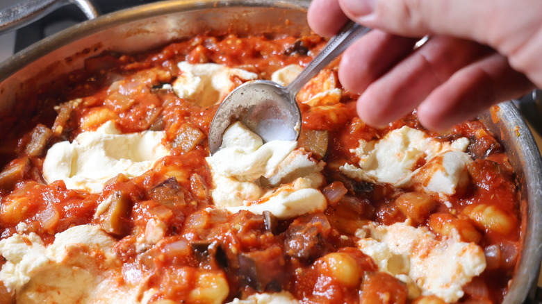 spoon adding ricotta to pan of gnocchi and eggplant in red sauce