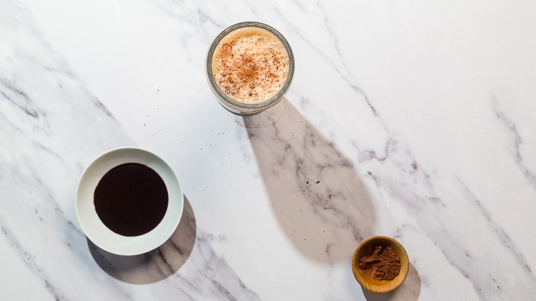 Glass with frothy egg cream, with pinch bowls of chocolate syrup and cocoa powder