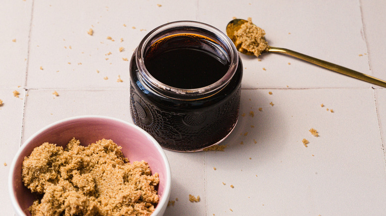 A bowl and a spoon of sugar next to a jar of syrup