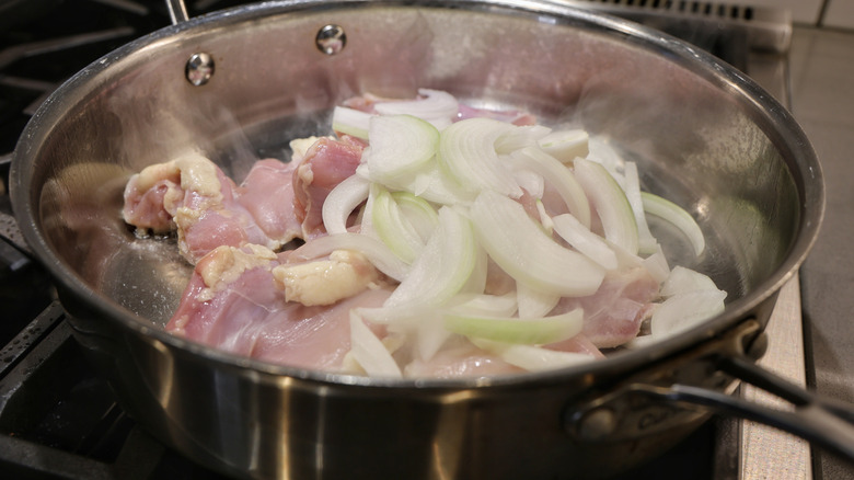 chicken thighs and sliced onions cooking in a stainless steel pan