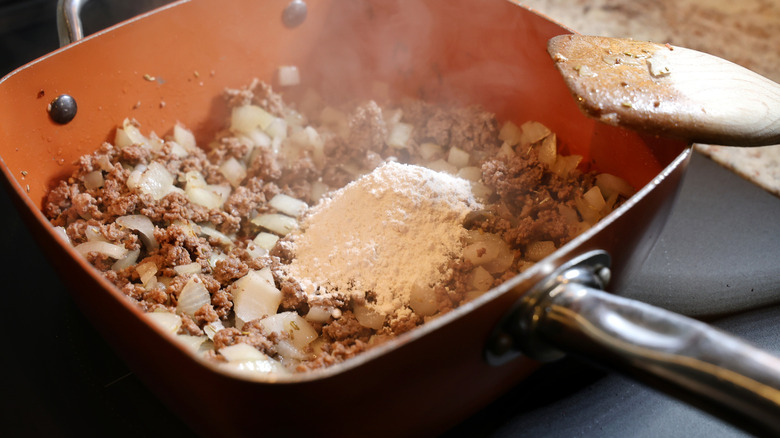 pile of flour atop cooking ground beef and onions in an orange pan