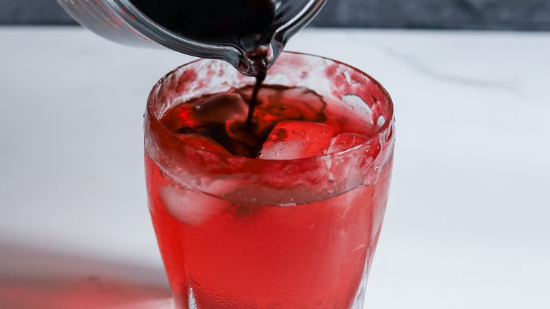 pouring black vodka into red cocktail