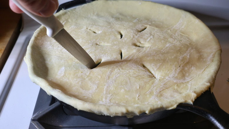 paring knife slicing steam vents into puff pastry on cast iron skillet