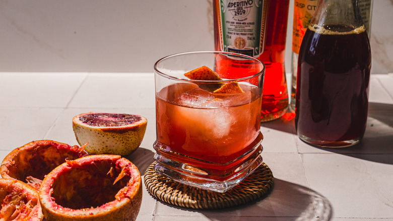 Overhead view of glass with blood orange Screwdriver cocktail alongside empty blood orange peels and bottles