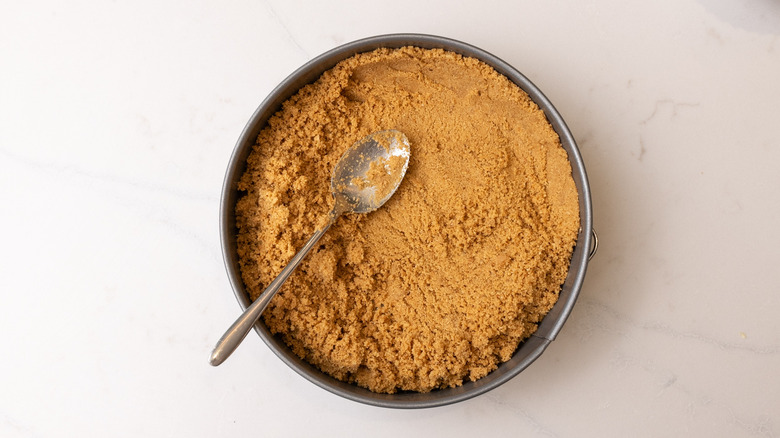 graham cracker pie crust mixture in a cake pan with spoon on top