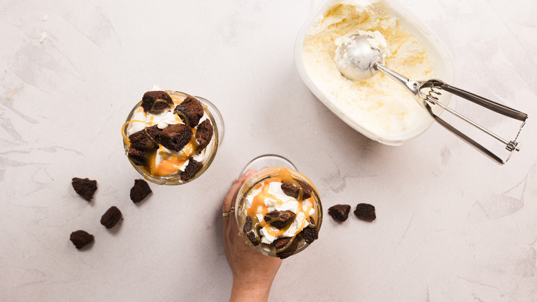 Hand holding one of two glasses with ice cream, caramel sauce and brownies