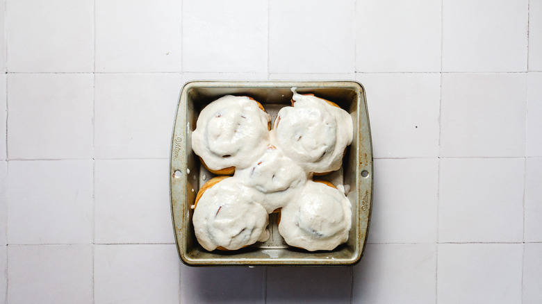 Tray of cinnamon buns topped with cream cheese spread