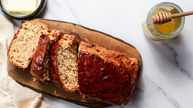 Sliced beer bread on cutting board near butter and honey