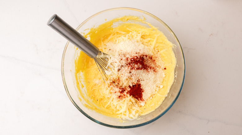 cornmeal mixture in bowl with Parmesan, grated cheddar, smoked paprika, and chili powder with whisk