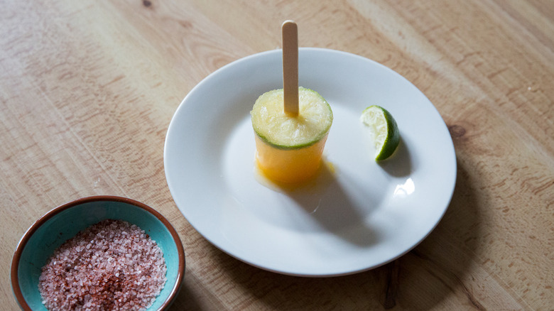 margarita popsicle and wedge of lime on white plate next to dish of salt rim