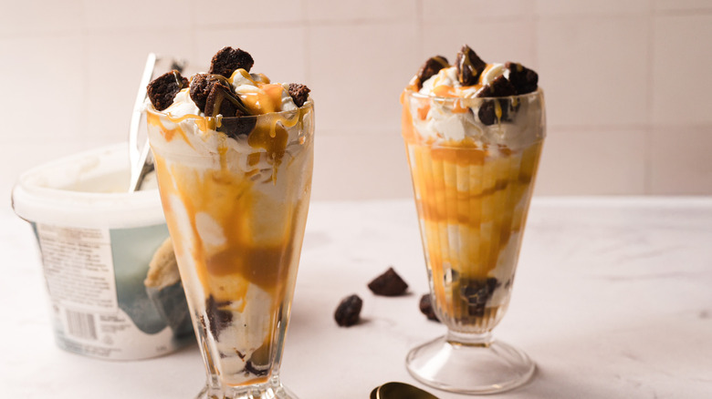 Two caramel brownie sundae with large vanilla ice cream pail and a scoop