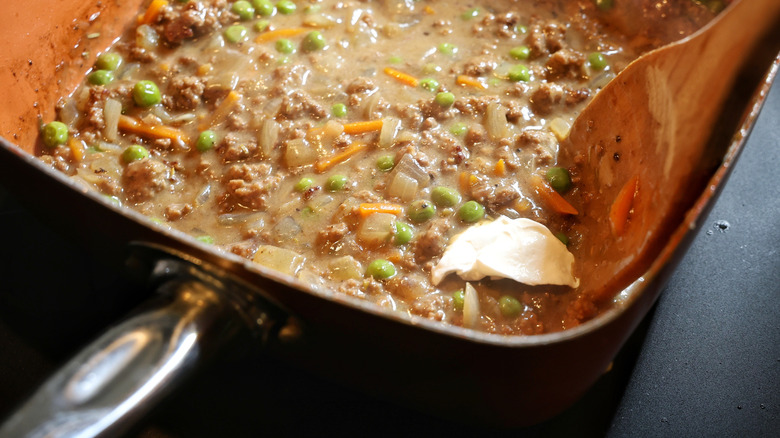 wooden spoon with dollop of sour cream in pan of beefy gravy