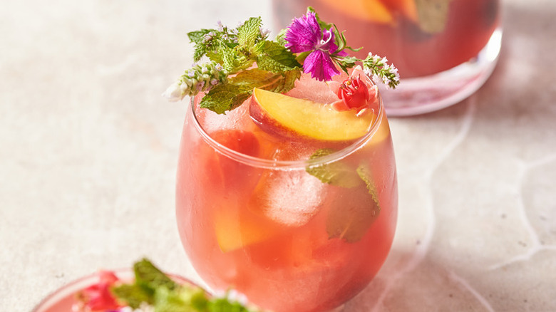 Watermelon sangria cocktail in a glass with peach slice and edible flower garnishes