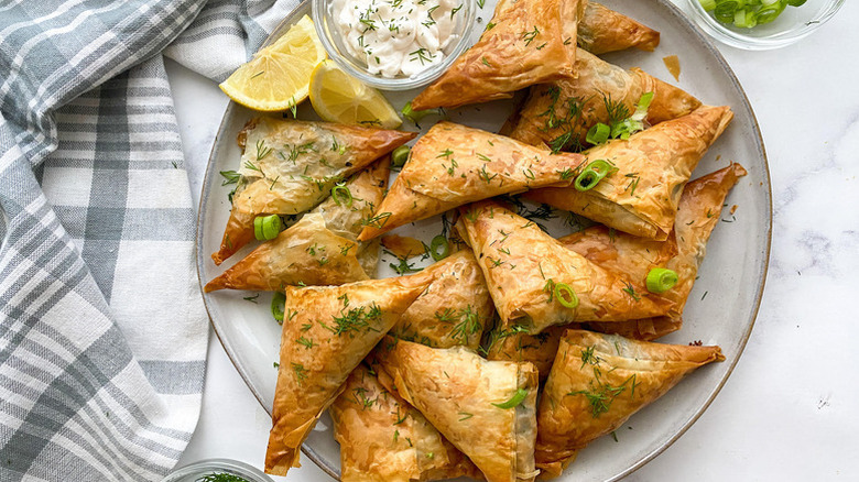 Individual spanakopita on plate with lemon wedges and creamy dip