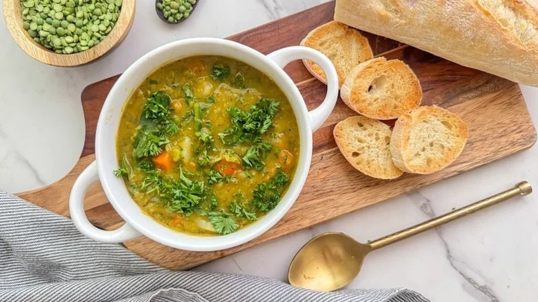 Bowl of split pea soup on wooden serving platter alongside sliced baguette