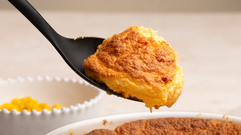 spoonful of cheesy corn souffle lingering over baked dish