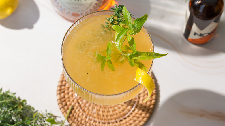Overhead view of yellow cocktail next to lemon verbena and lemon and liqueur bottles