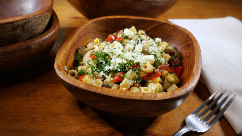 a wooden bowl of cowboy caviar pasta salad with a fork and napkin beside it