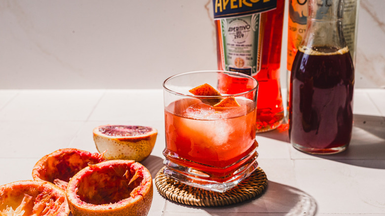 Side view of glass with blood orange screwdriver cocktail alongside empty blood orange peels and bottles
