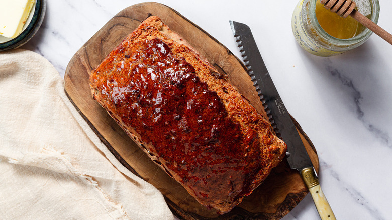 Whole beer bread on cutting board with knife near butter and honey