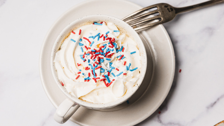 A mug cake with whipped cream and sprinkles and a fork