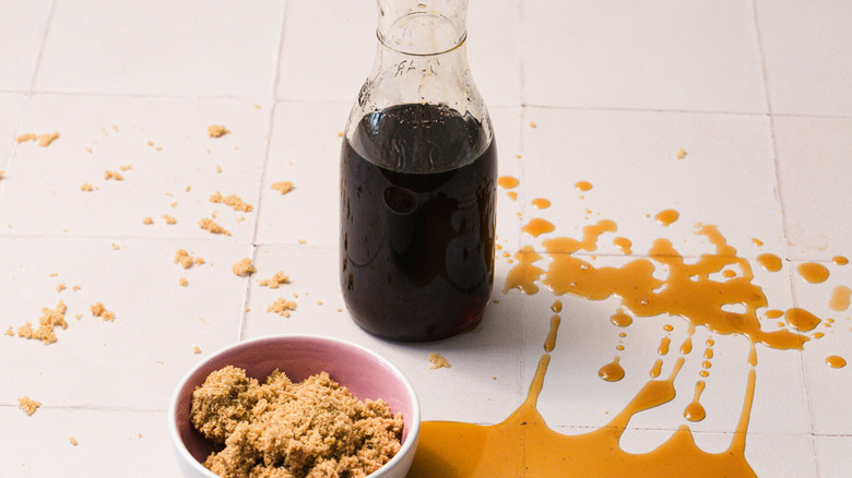 Small bowl of brown sugar next to carafe with brown sugar syrup and some spilled